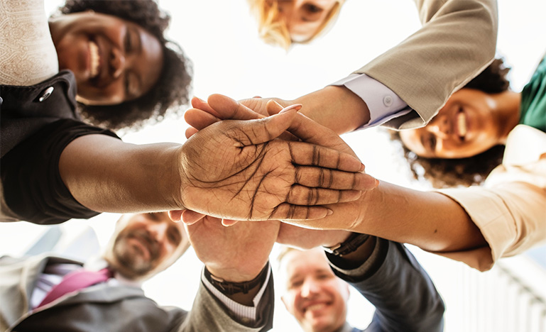 Diverse group of people standing in a circle with their hands in the middle